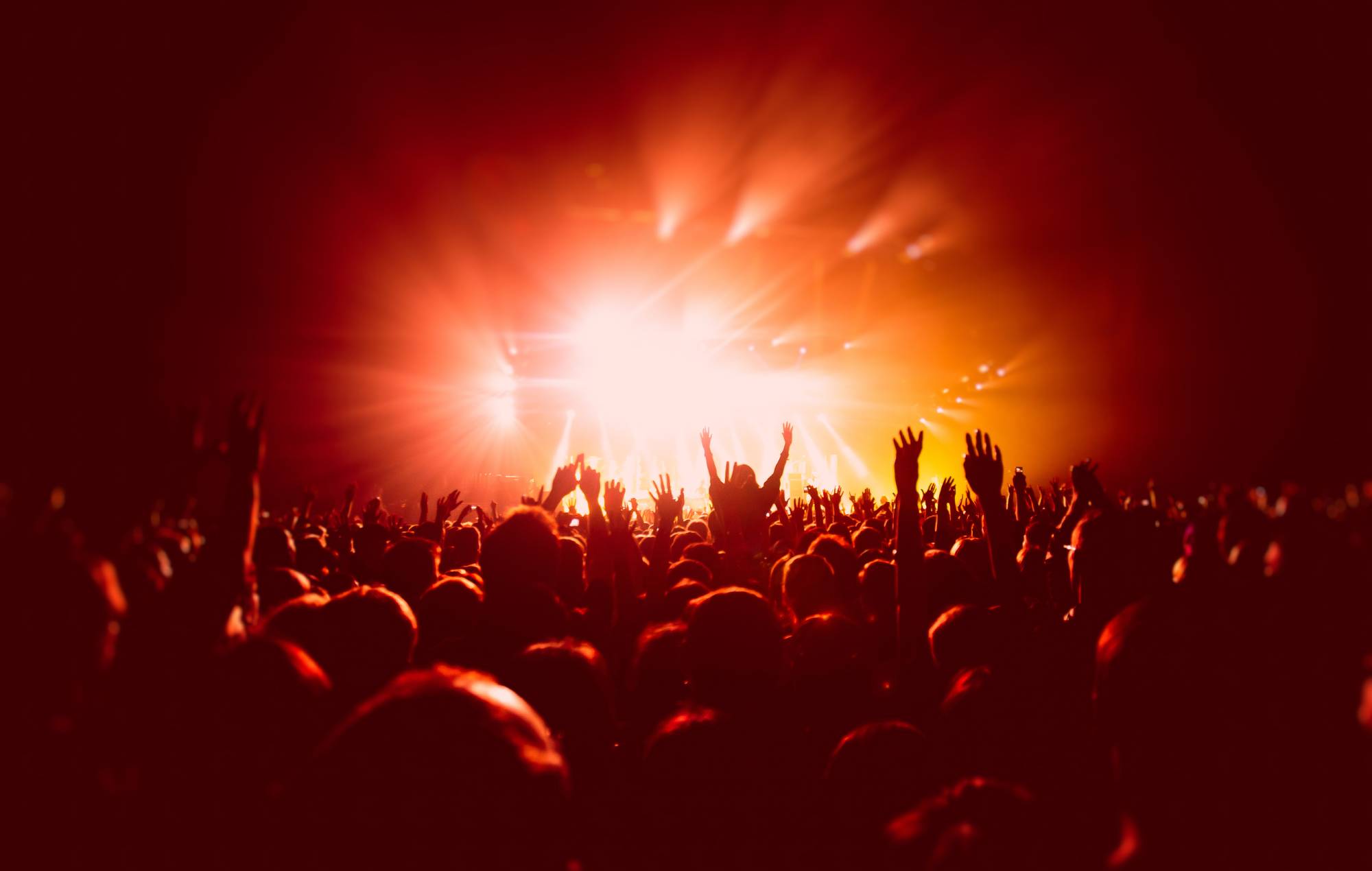 A crowded concert hall with scene stage in red lights, rock show performance, with people silhouette, colourful confetti explosion fired on dance floor during a concert festival. Credit: Nikolay Tsuguliev